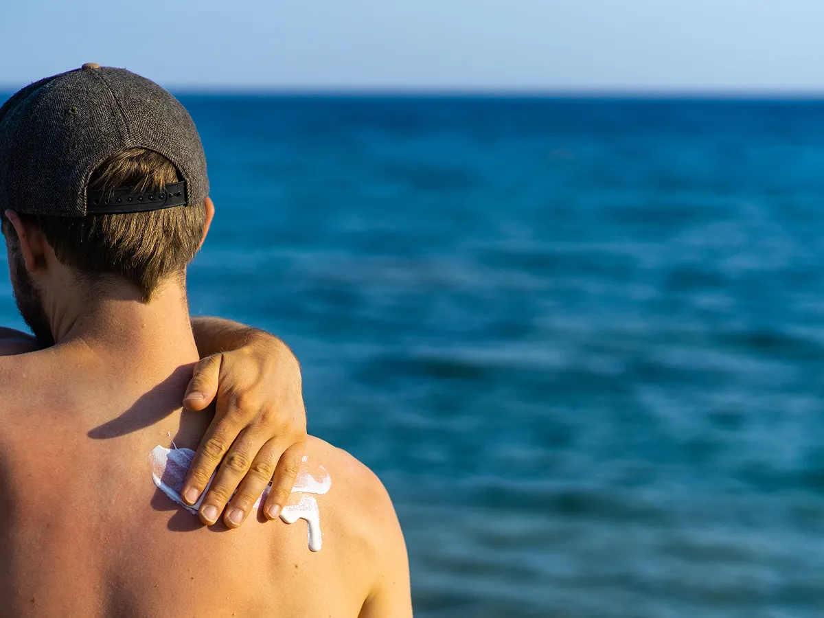 Man applying sunscreen on his back with beach view