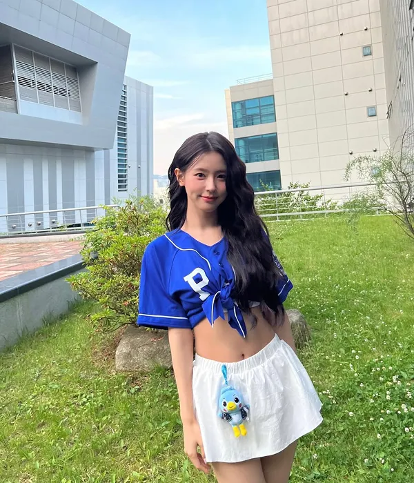 G-IDLE Miyeon wearing a blue cropped baseball shirt and white skirt with long, wavy hair